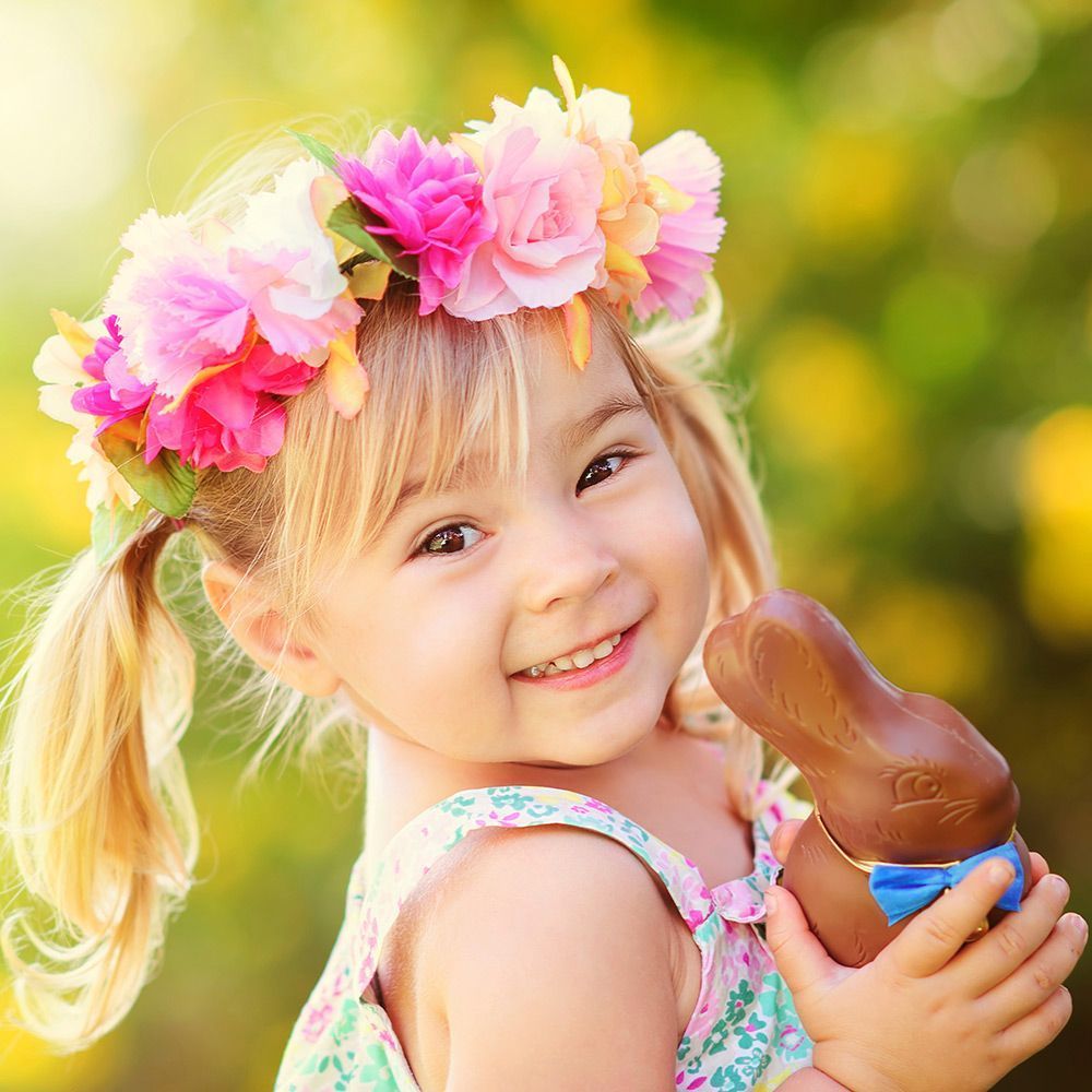 Kleines Mädchen mit Blumenkranz auf dem Kopf mit Schokoladenosterhase