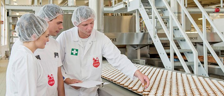 3 Mitarbeiter begutachten die am Laufband hergestellten Lebkuchen